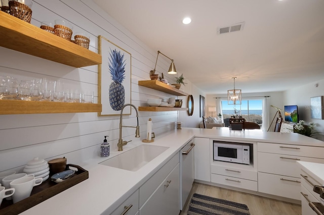 kitchen with kitchen peninsula, white microwave, sink, pendant lighting, and white cabinets