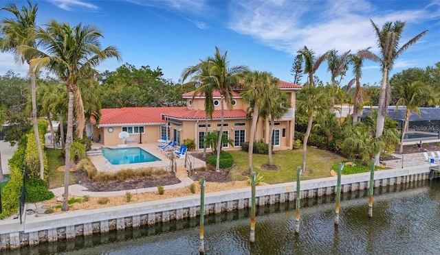 rear view of property featuring a water view, a tiled roof, stucco siding, a yard, and a patio area