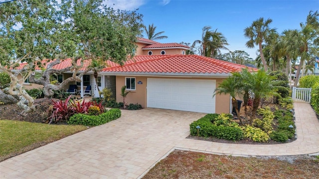 mediterranean / spanish-style house featuring fence, stucco siding, a garage, a tile roof, and decorative driveway