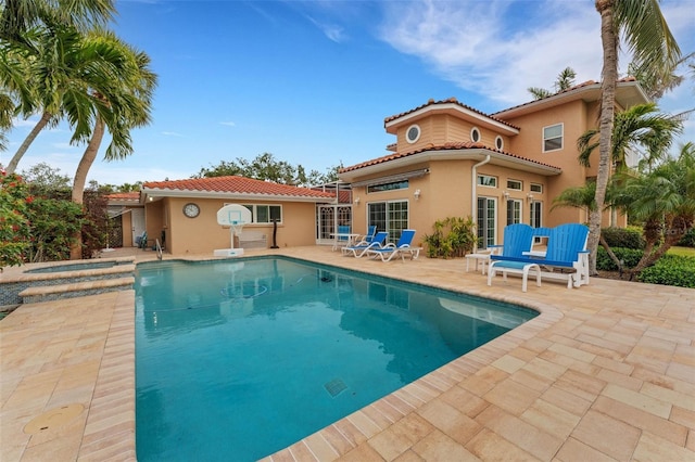 rear view of property with a patio, an outdoor pool, a tile roof, and stucco siding