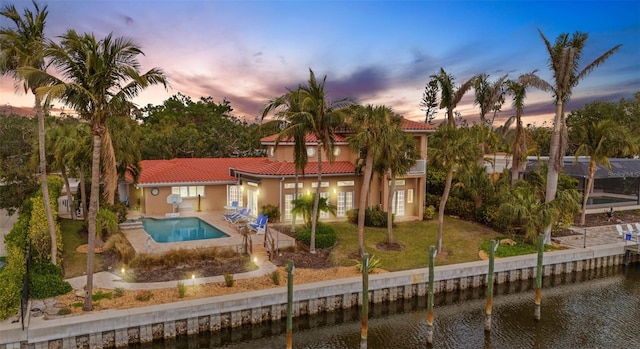 back house at dusk with a water view, a fenced in pool, a patio area, and a lawn