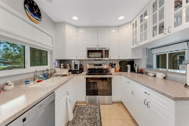 kitchen with light stone countertops, light tile patterned flooring, appliances with stainless steel finishes, and white cabinets