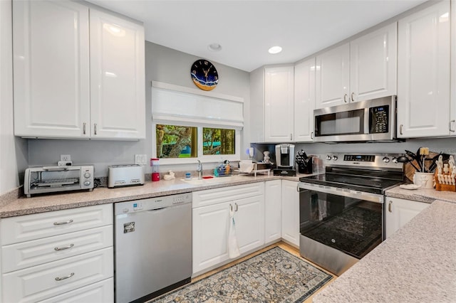kitchen featuring a toaster, light countertops, stainless steel appliances, white cabinetry, and a sink