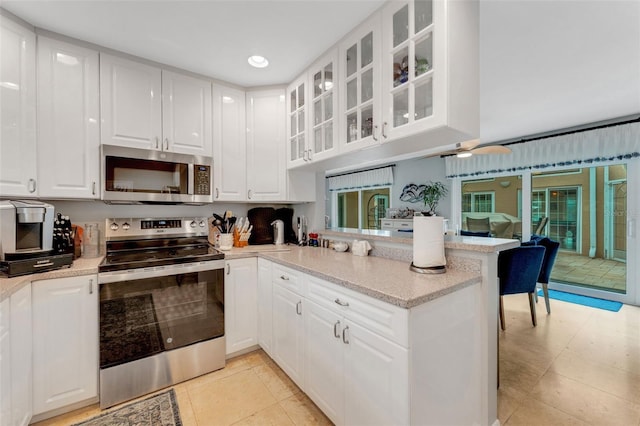 kitchen with a peninsula, white cabinets, light stone countertops, and stainless steel appliances