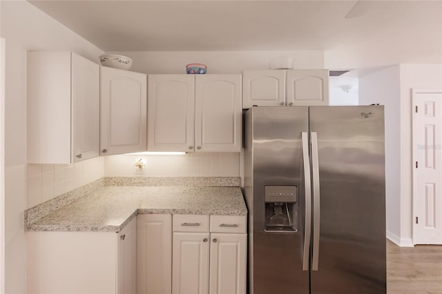 kitchen featuring stainless steel fridge with ice dispenser, white cabinetry, tasteful backsplash, light hardwood / wood-style flooring, and light stone counters