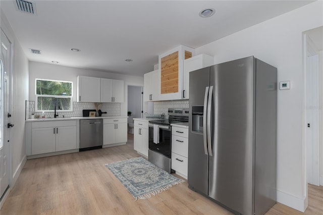 kitchen with appliances with stainless steel finishes, tasteful backsplash, sink, light hardwood / wood-style flooring, and white cabinetry