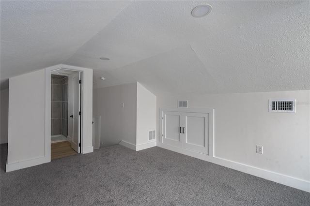 additional living space with vaulted ceiling, dark carpet, and a textured ceiling