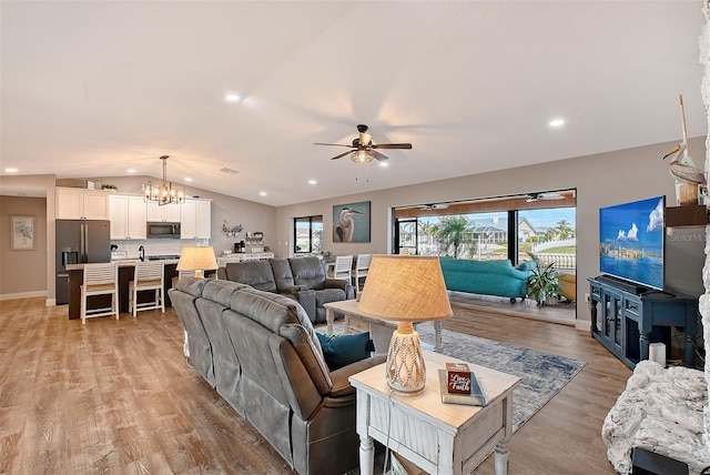 living room featuring light wood-type flooring, ceiling fan with notable chandelier, and lofted ceiling