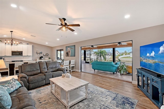 living room featuring ceiling fan with notable chandelier, light hardwood / wood-style flooring, and vaulted ceiling