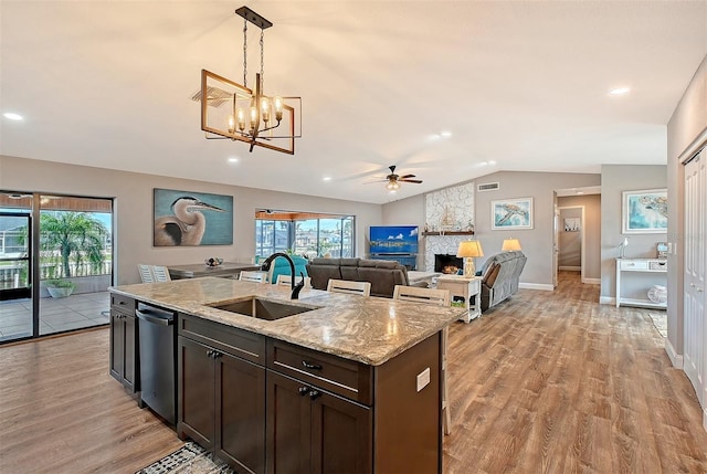 kitchen with sink, a stone fireplace, light stone counters, pendant lighting, and dark brown cabinets