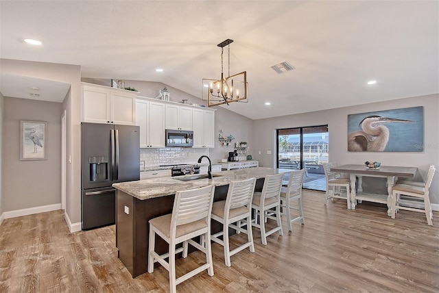 kitchen featuring a kitchen island with sink, white cabinets, decorative backsplash, appliances with stainless steel finishes, and light stone counters