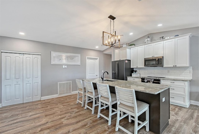 kitchen featuring white cabinets, pendant lighting, stainless steel appliances, and a kitchen island with sink