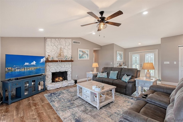 living room with wood-type flooring, vaulted ceiling, a stone fireplace, and ceiling fan