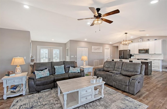 living room featuring french doors, ceiling fan with notable chandelier, light hardwood / wood-style flooring, and lofted ceiling