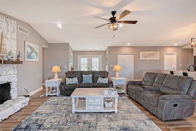 living room featuring ceiling fan, a stone fireplace, dark wood-type flooring, and vaulted ceiling