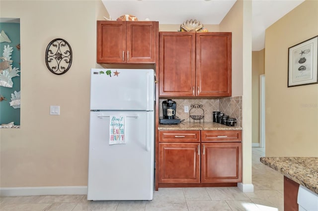 kitchen with light stone countertops, decorative backsplash, white fridge, and light tile patterned flooring