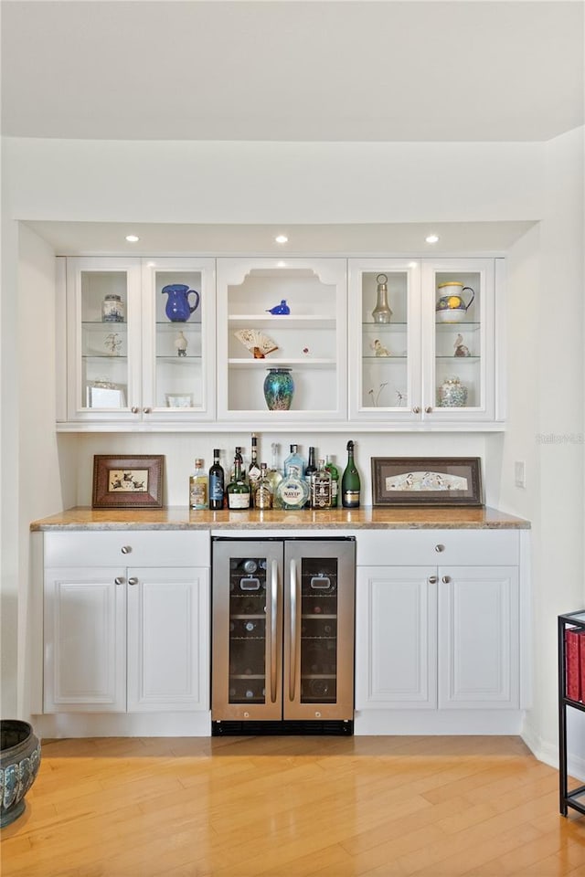 bar featuring light hardwood / wood-style floors, light stone countertops, white cabinets, and wine cooler