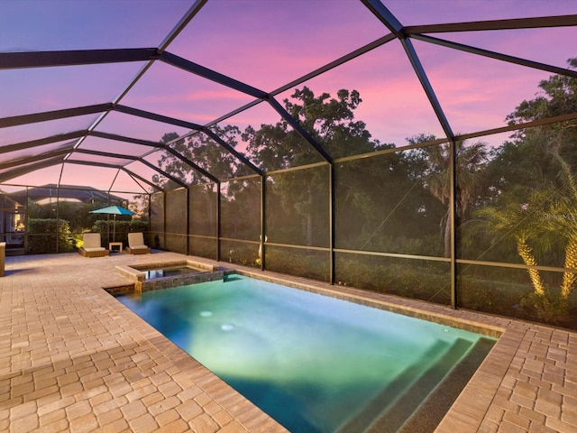 pool at dusk featuring glass enclosure, an in ground hot tub, and a patio area