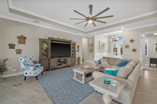 living room featuring ceiling fan with notable chandelier, a raised ceiling, ornamental molding, and light tile patterned floors