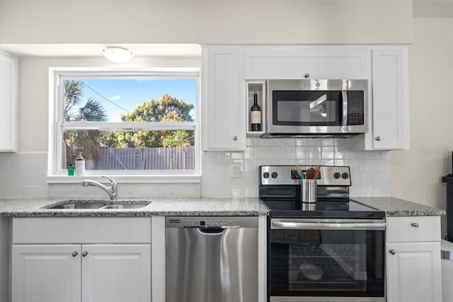 kitchen featuring tasteful backsplash, light stone counters, stainless steel appliances, sink, and white cabinets