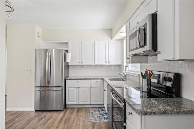 kitchen with sink, stainless steel appliances, dark stone counters, white cabinets, and light wood-type flooring