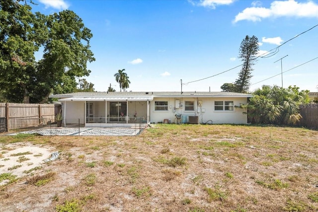 rear view of property with a lawn, central air condition unit, and a sunroom