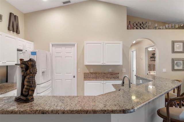 kitchen featuring lofted ceiling, white fridge with ice dispenser, light stone countertops, and white cabinets