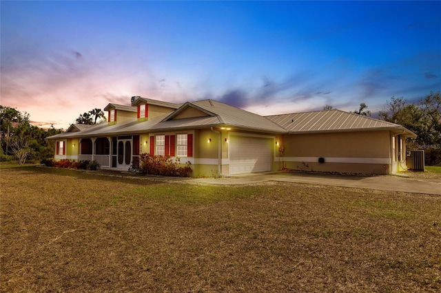 back house at dusk featuring a garage, a yard, and central air condition unit