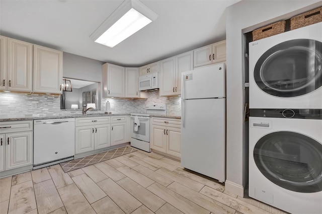 kitchen featuring white appliances, light stone counters, stacked washer / dryer, and sink