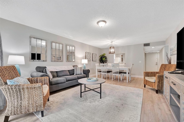 living room with a textured ceiling, a notable chandelier, and light hardwood / wood-style flooring