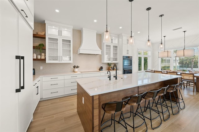 kitchen featuring white cabinets, custom range hood, decorative light fixtures, and a large island