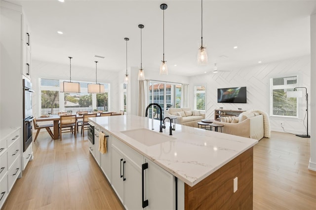 kitchen featuring pendant lighting, white cabinetry, sink, and a kitchen island with sink