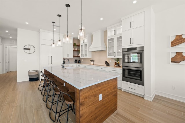 kitchen with white cabinets, a large island with sink, stainless steel double oven, and custom exhaust hood