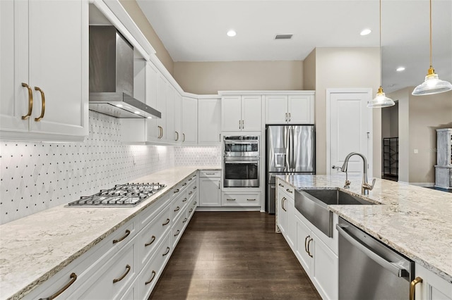 kitchen with wall chimney exhaust hood, white cabinetry, stainless steel appliances, sink, and hanging light fixtures