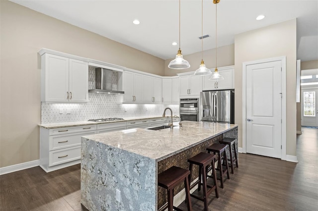 kitchen with appliances with stainless steel finishes, wall chimney exhaust hood, white cabinetry, sink, and a center island with sink