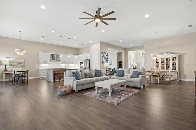 living room with dark hardwood / wood-style flooring, ceiling fan with notable chandelier, and sink