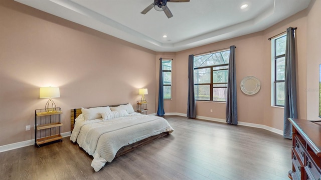 bedroom with ceiling fan, dark hardwood / wood-style flooring, and a tray ceiling