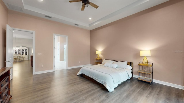 bedroom with ceiling fan, dark wood-type flooring, and a tray ceiling