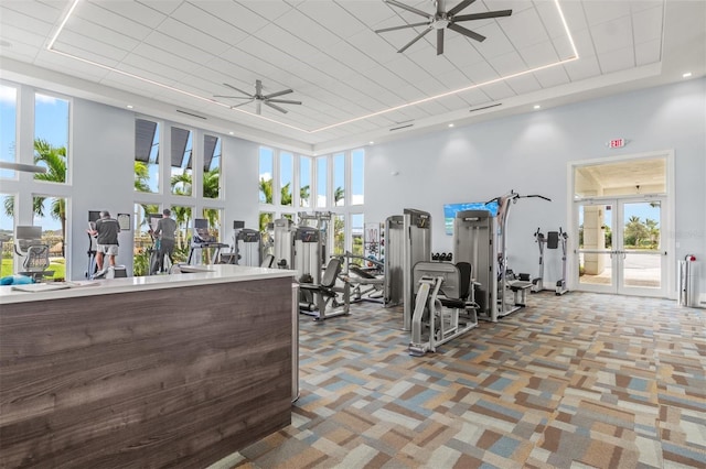 workout area with ceiling fan, a raised ceiling, a towering ceiling, french doors, and carpet flooring