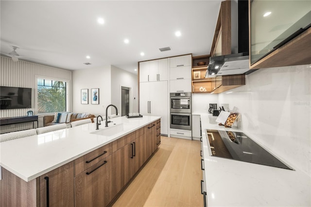 kitchen featuring stainless steel double oven, black electric cooktop, sink, wall chimney range hood, and white cabinets