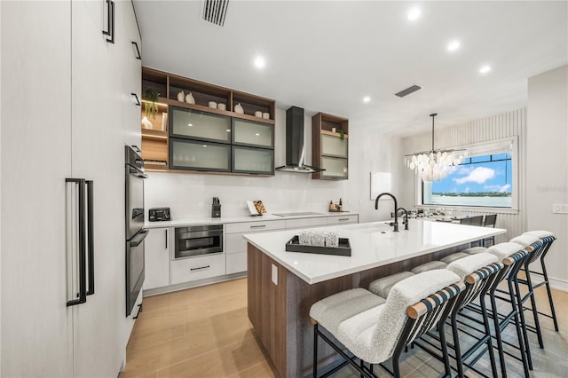 kitchen featuring wall chimney exhaust hood, sink, pendant lighting, white cabinetry, and an island with sink