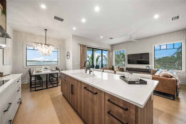 kitchen featuring a kitchen island with sink, ceiling fan with notable chandelier, sink, light hardwood / wood-style flooring, and white cabinetry