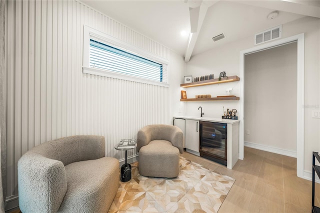 sitting room with light hardwood / wood-style floors, beamed ceiling, beverage cooler, and indoor wet bar