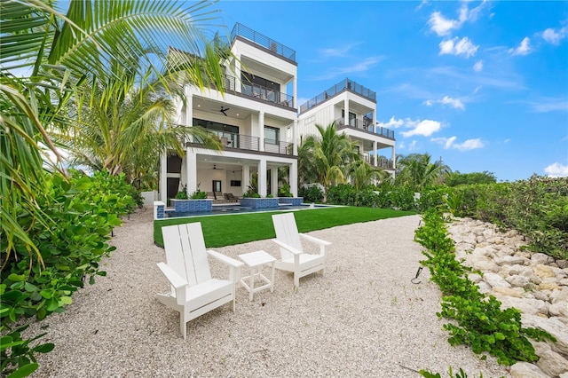 back of property with ceiling fan, a balcony, a yard, and a patio