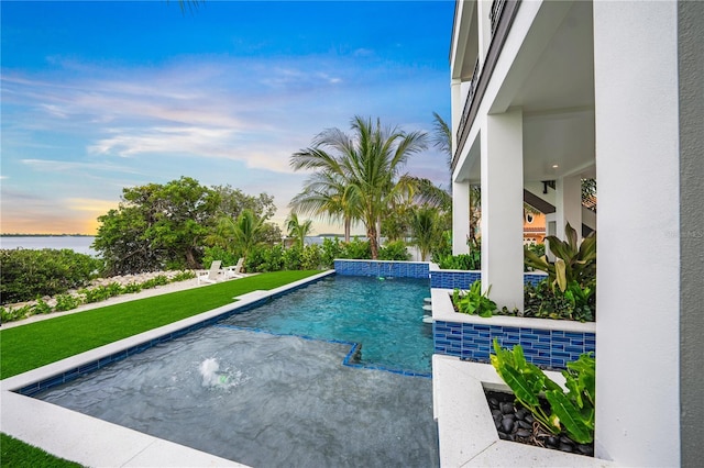 pool at dusk with a lawn, pool water feature, and a water view