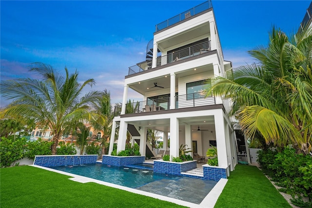 rear view of house with ceiling fan, a yard, pool water feature, a balcony, and a patio