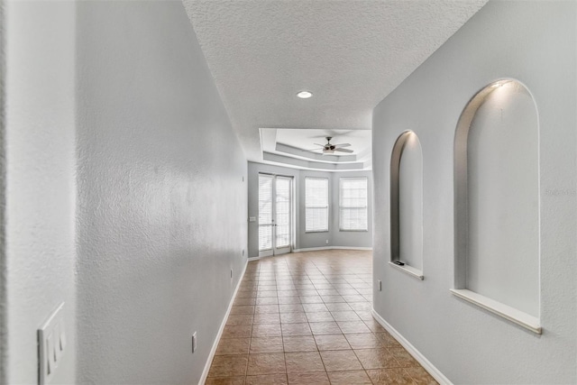 hall with tile patterned floors, a raised ceiling, and a textured ceiling