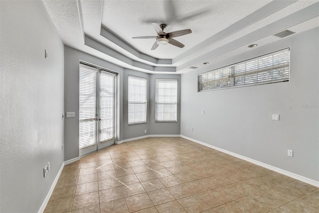 empty room with light tile patterned flooring, ceiling fan, a healthy amount of sunlight, and a tray ceiling