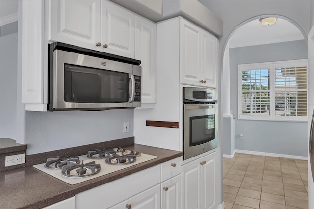 4708 Clipper Dr, Bradenton, FL 34208 - kitchen with light tile patterned flooring, arched walkways, dark countertops, stainless steel appliances, and white cabinets