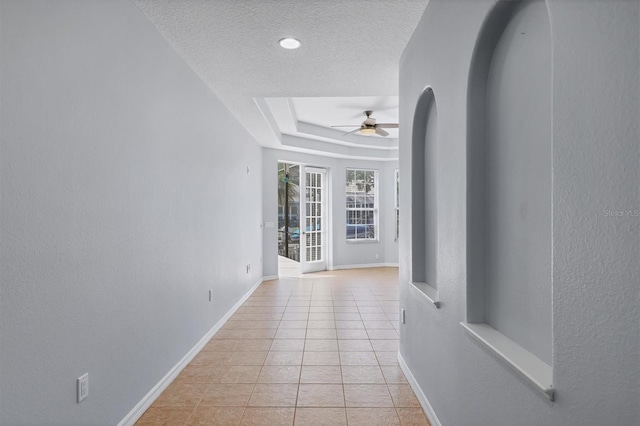 4708 Clipper Dr, Bradenton, FL 34208 - corridor featuring light tile patterned floors, a tray ceiling, a textured ceiling, baseboards, and arched walkways